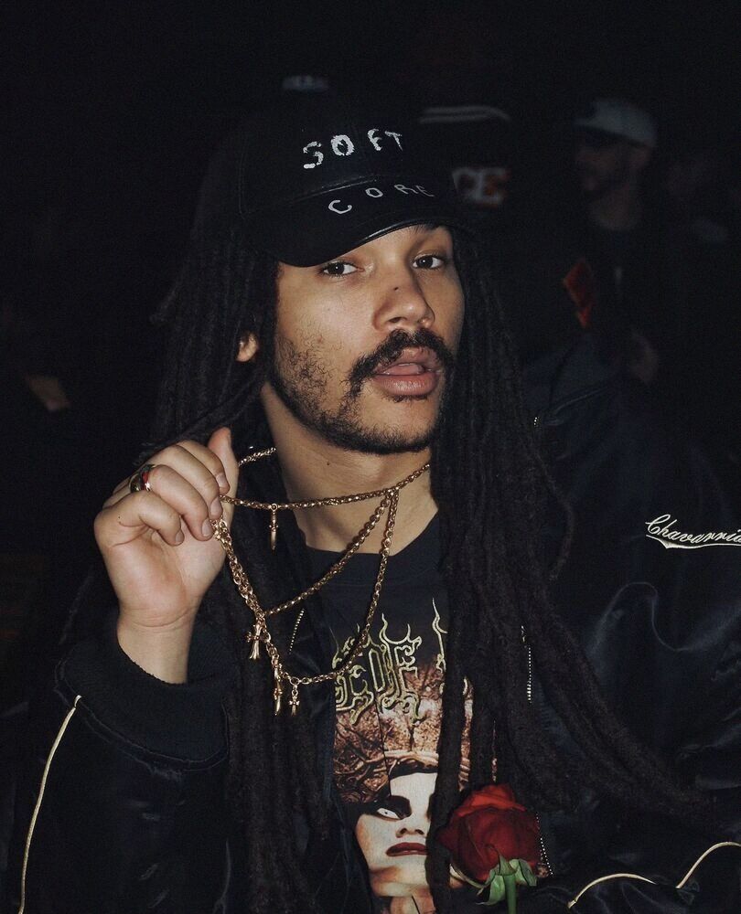 Man with locs and a cap holding a rose