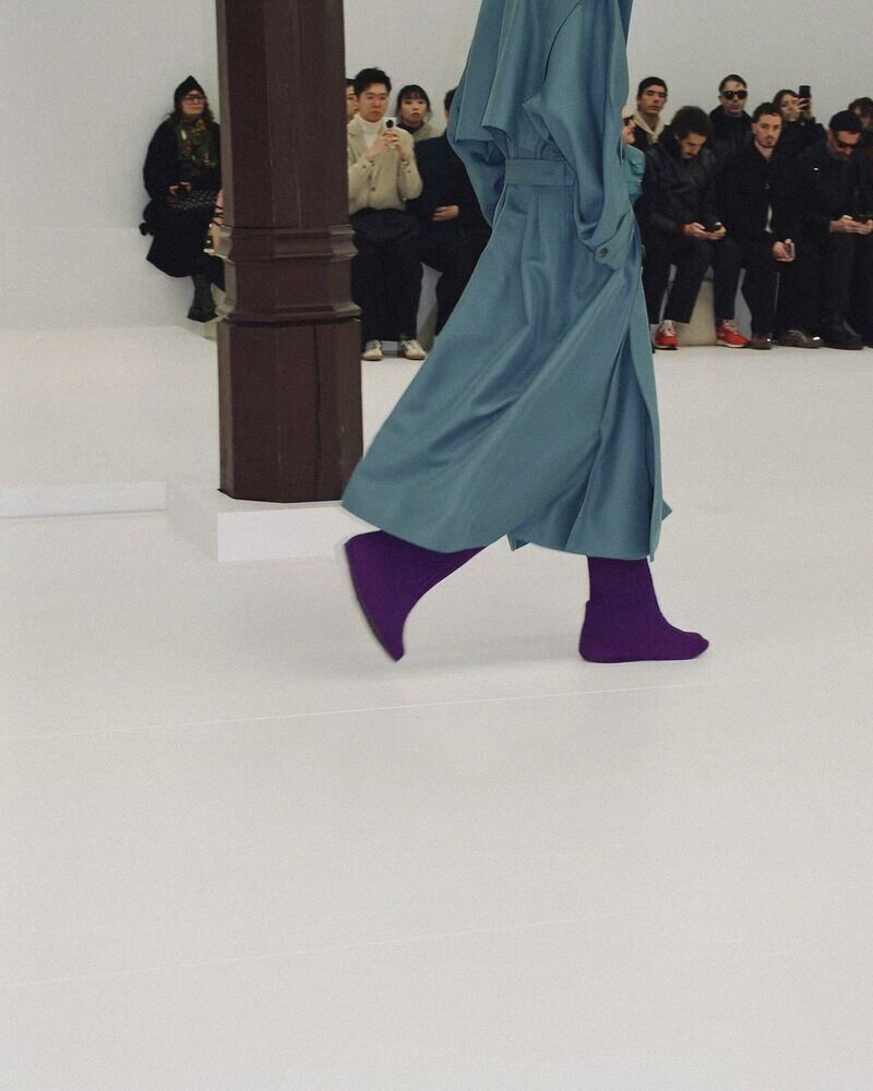 Model in a teal coat and purple boots on a white runway