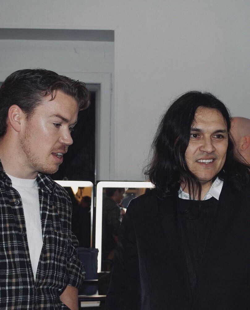Two men talking backstage by the mirrors
