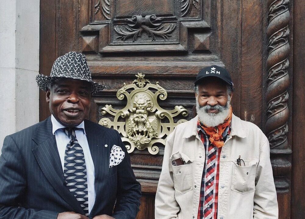 Two older men in suits in front of an ornate door