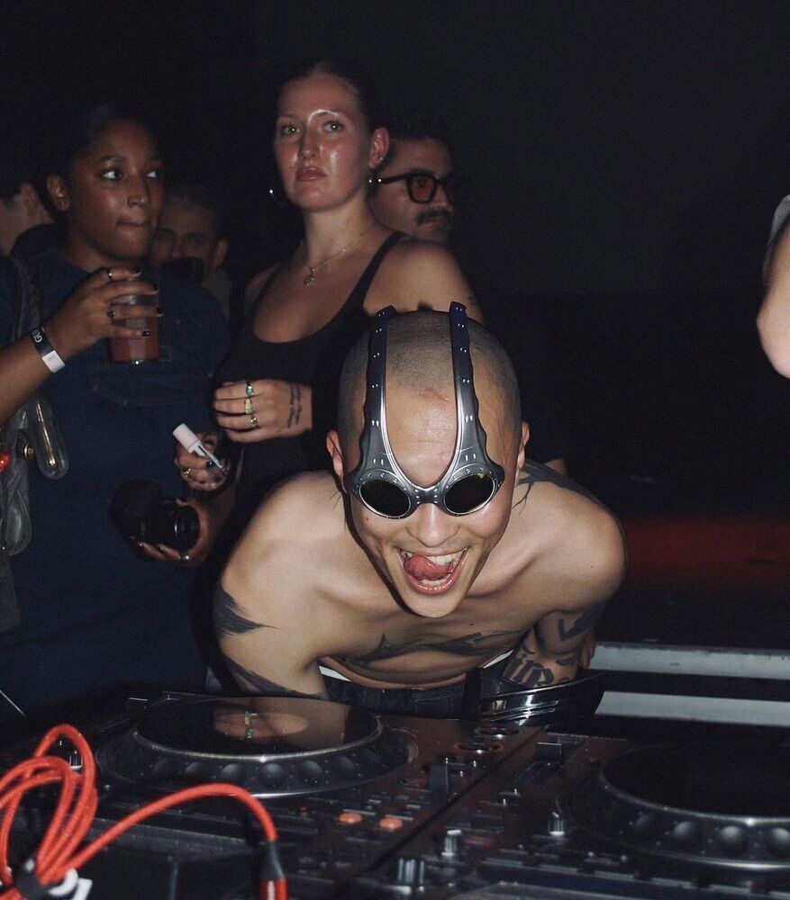DJ in sculptural goggles leaning over decks